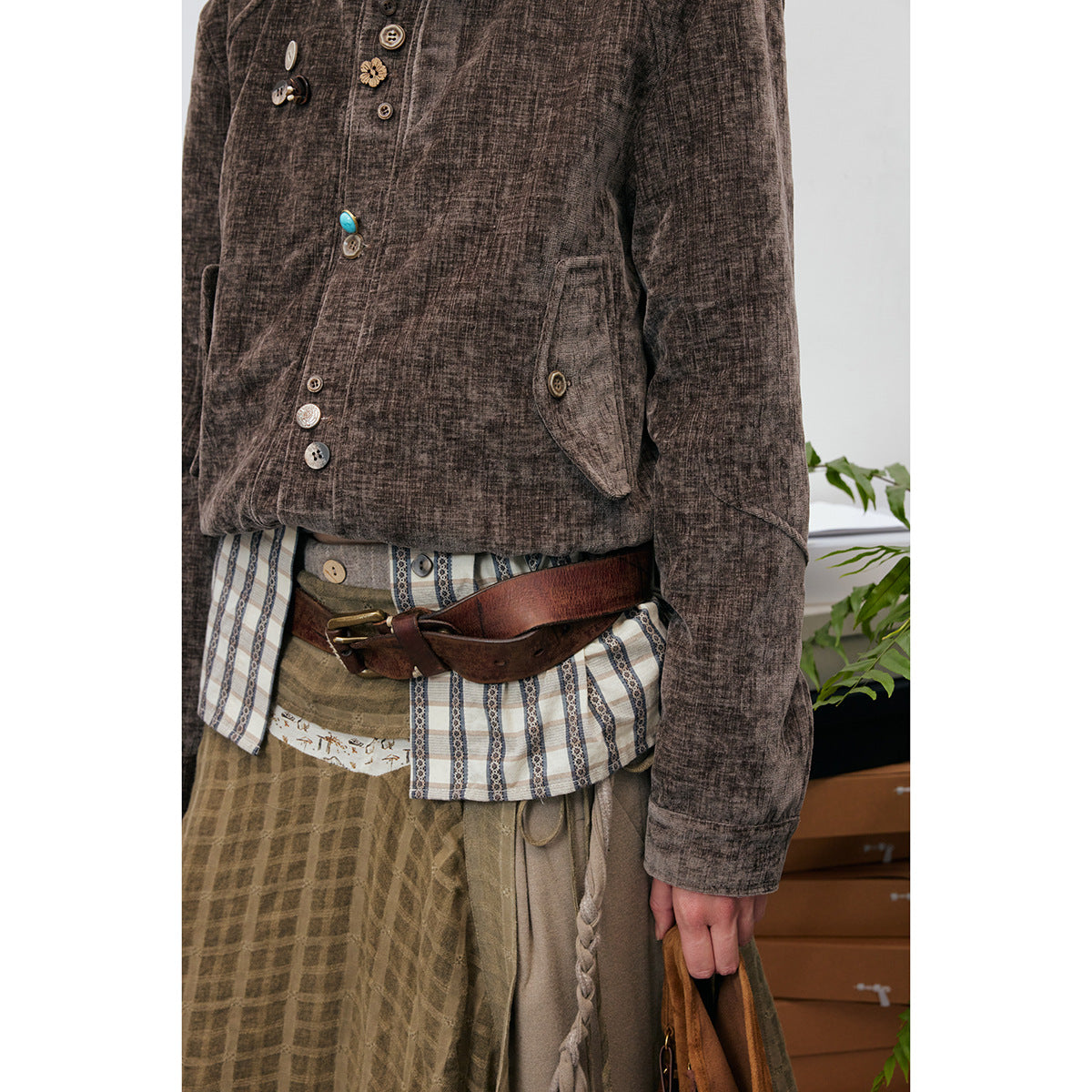 Close view of the brown jacket's buttons and pockets, layered striped shirt, and wide leather belt.