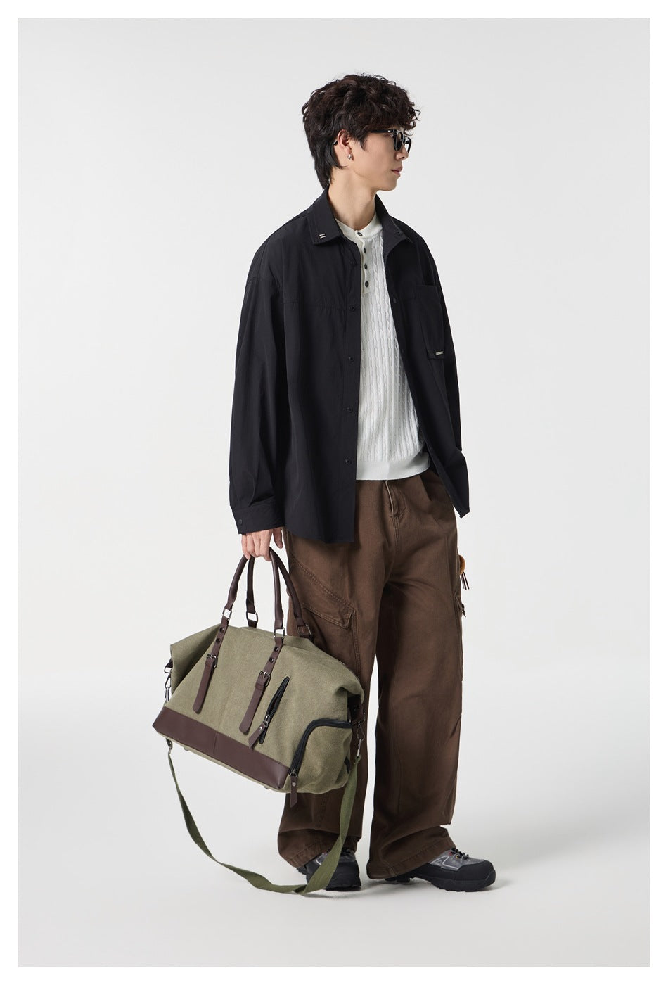 Side-view model wearing a black button-front shirt over a white knit top, holding a large olive and brown bag.