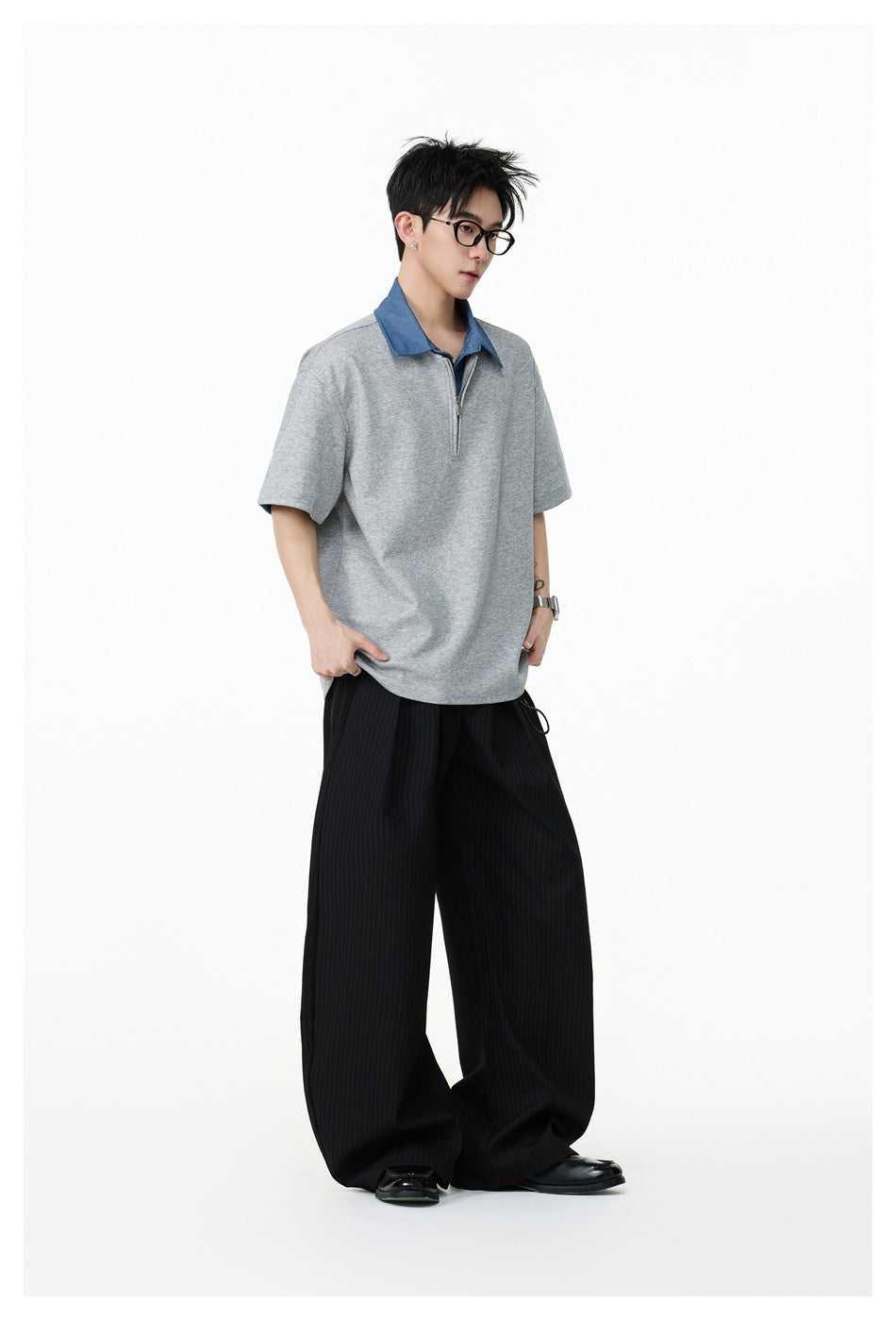 Three-quarter view of a model wearing a gray short-sleeve top with a blue collar and quarter zip, and black wide-leg