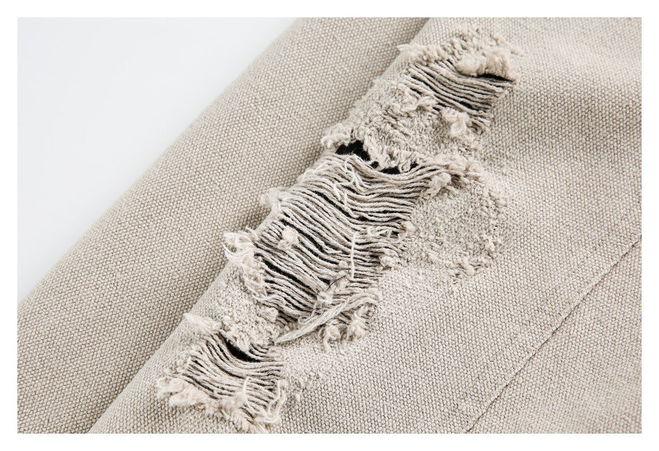 Close-up of a light beige garment with a heavily frayed, distressed fabric detail.