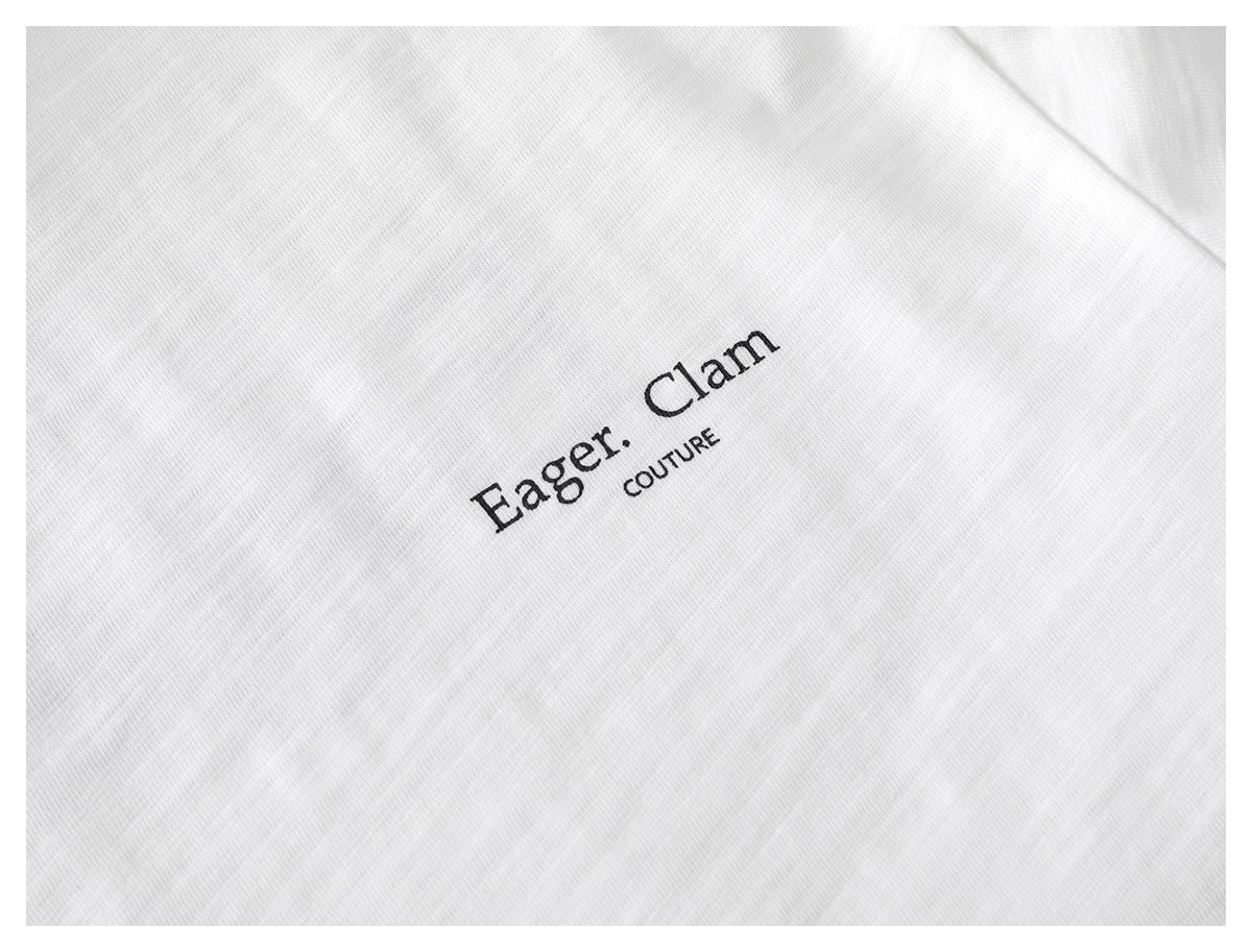 Close-up of black “Eager. Clam” and “COUTURE” lettering printed on white T-shirt fabric.