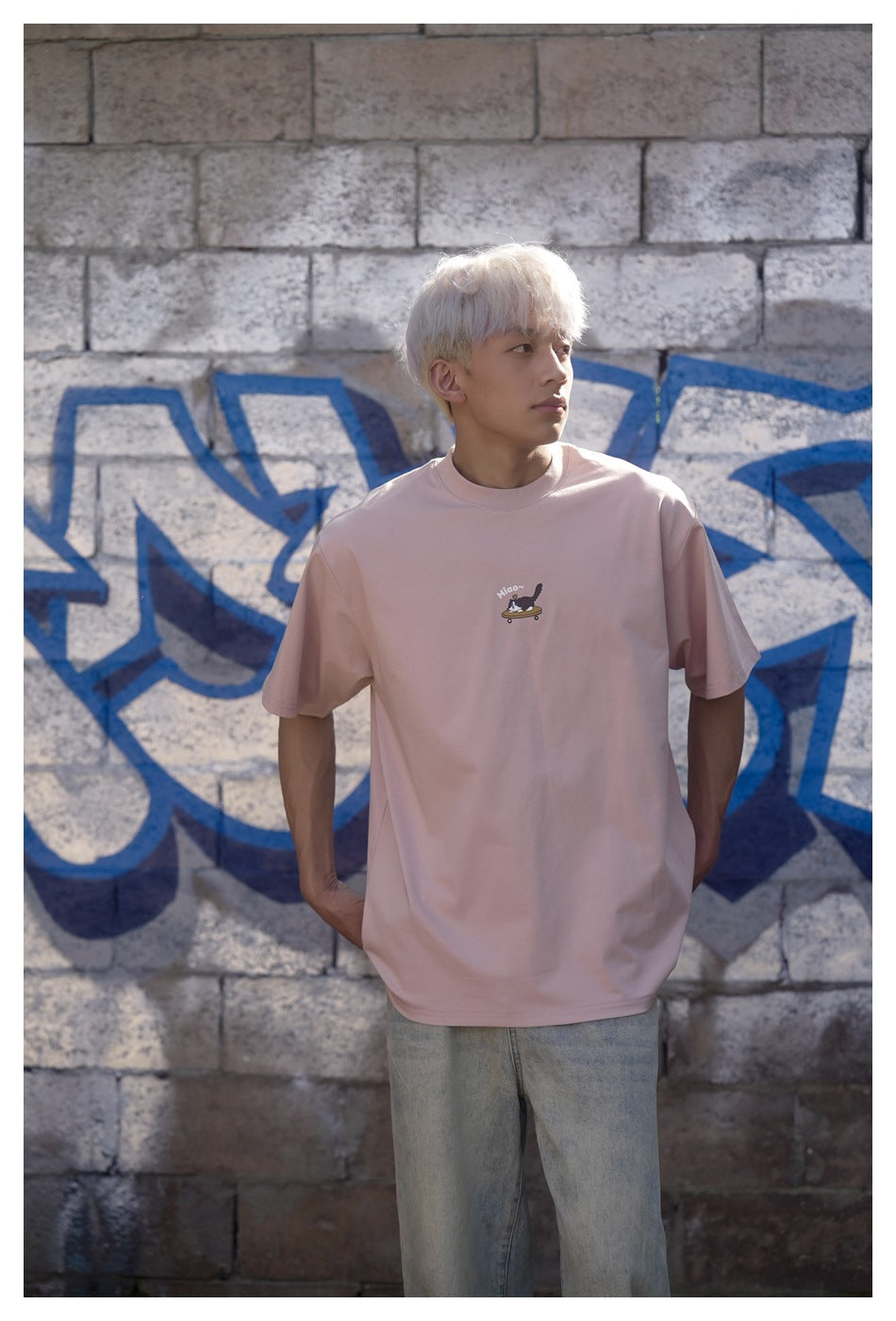 Front view of a model wearing a pale pink oversized T-shirt with a small cat-on-skateboard chest graphic.