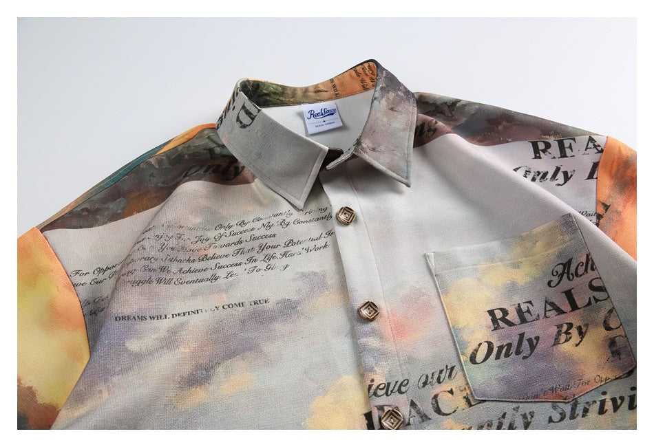 Partial front view of a laid-flat collared shirt with a chest pocket and multicolored cloudy print with black lettering.