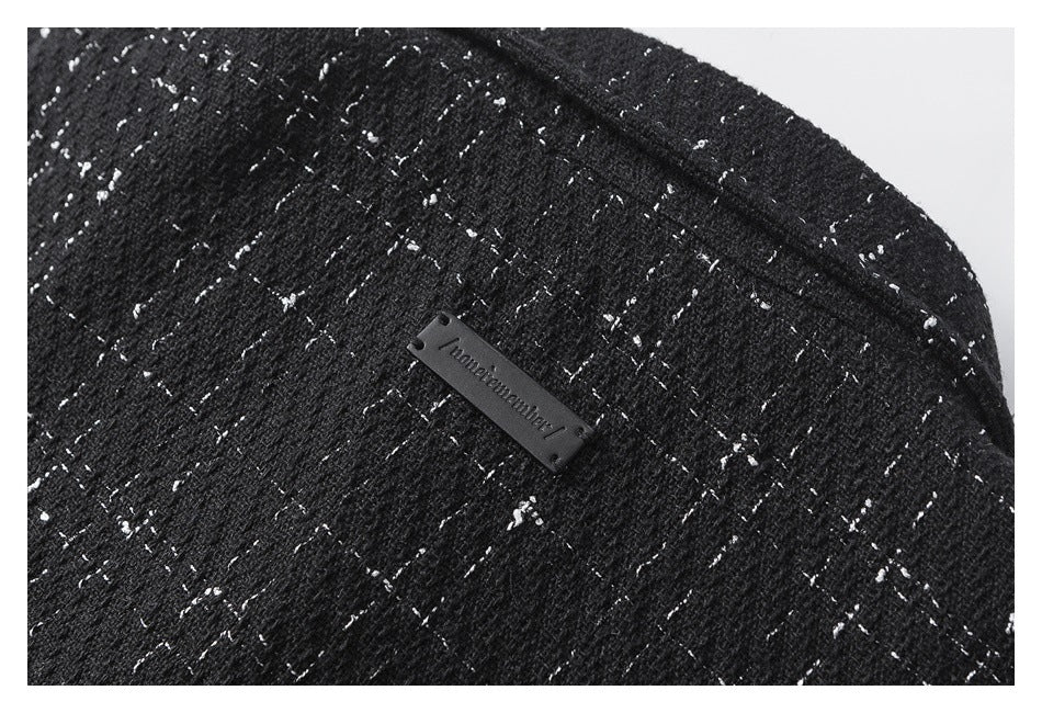 Close-up of black fabric with white flecks and a small dark rectangular brand label.
