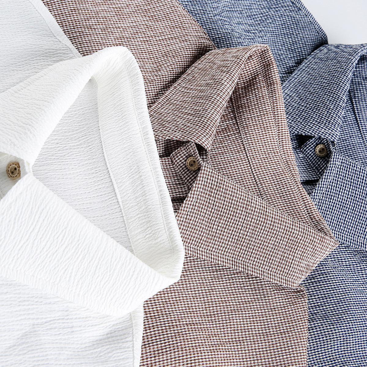 Close-up of white, brown-check, and blue-check short-sleeve shirts showing their collars and buttons.