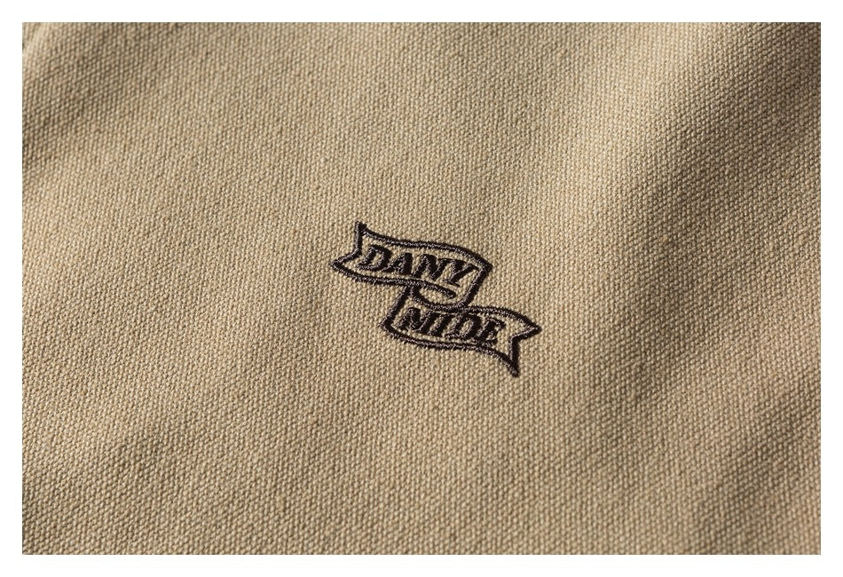 Close-up of dark embroidered lettering on beige textured garment fabric.
