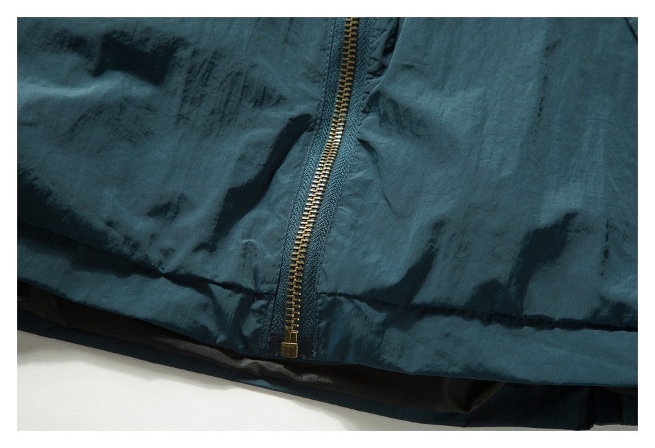 Close-up of a brass-colored zipper along the hem of a dark teal garment.