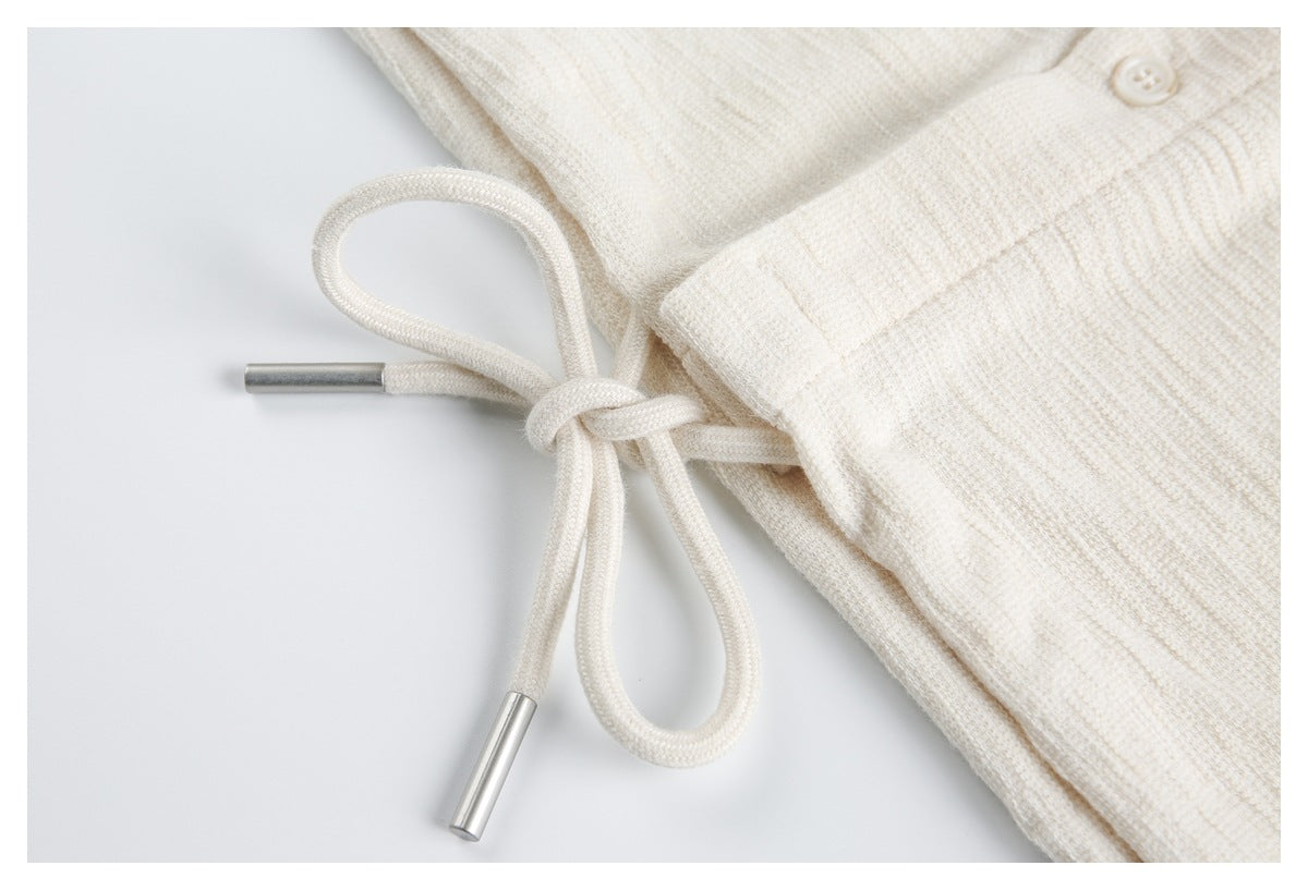 Close-up of an ivory drawstring with silver-colored tips at the edge of a textured garment.