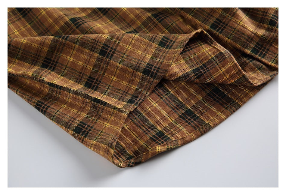 Close-up of the plaid shirt’s curved hem and stitched edge laid against a light background.