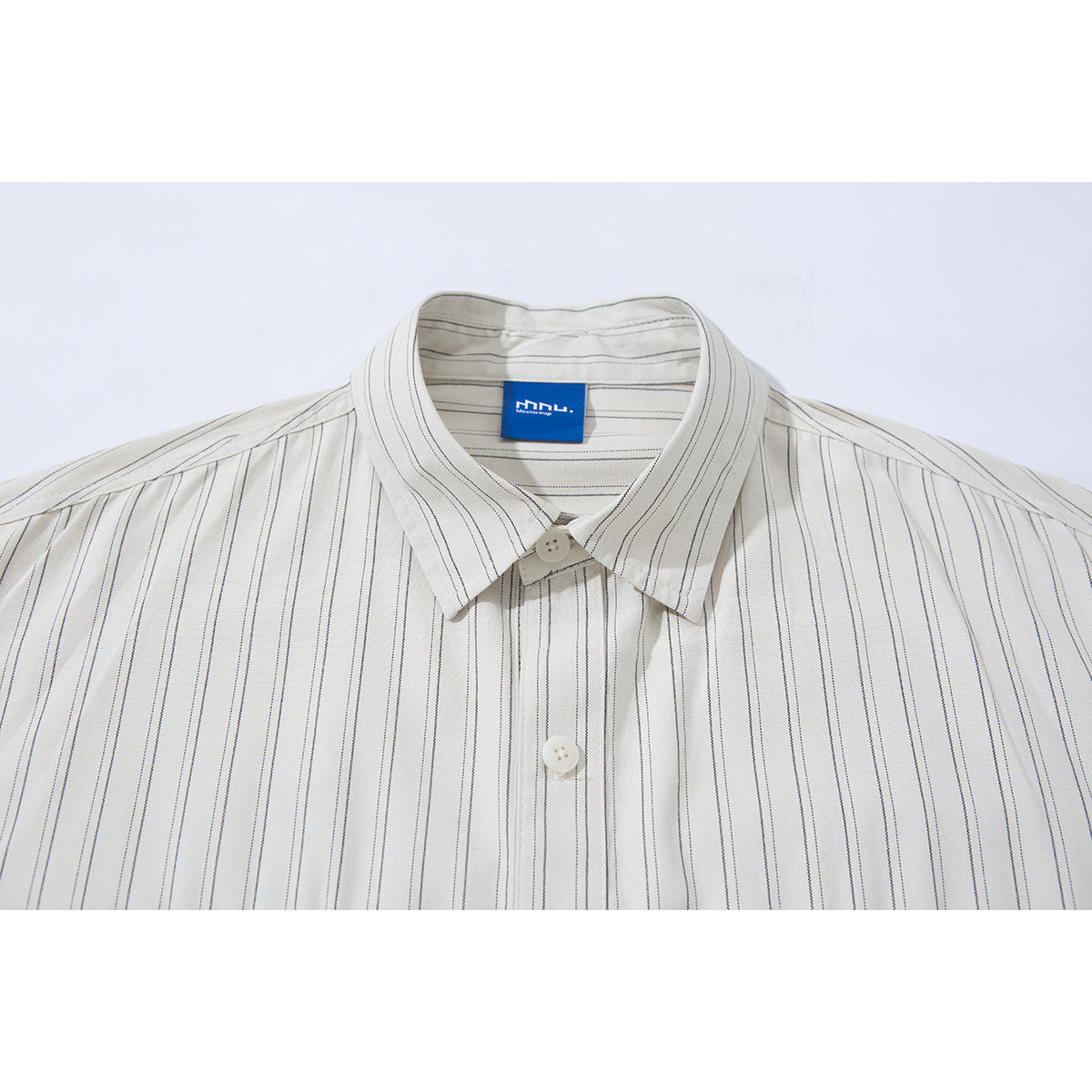 Close-up of an off-white shirt with thin dark vertical stripes, pointed collar, buttons and a blue neck label.