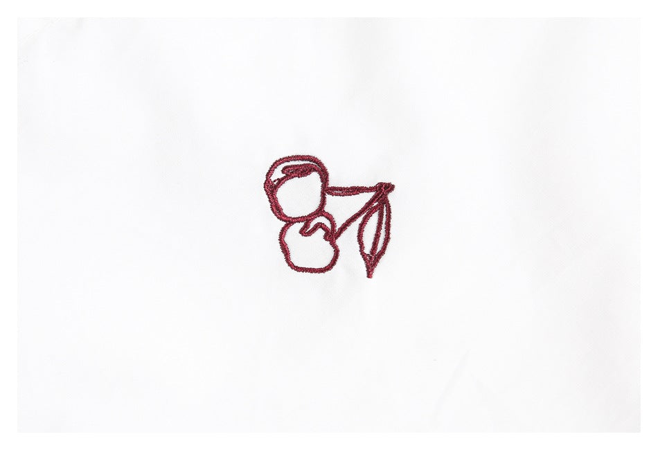 Close-up of a red embroidered cherry motif on white shirt fabric.