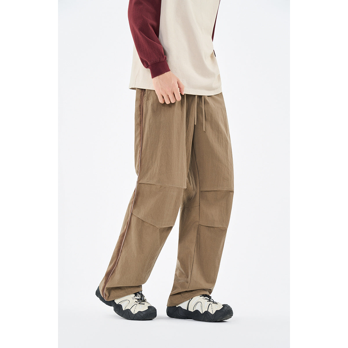Model wearing loose tan trousers with contrast side piping and paneled knees, shown from the front at an angle.