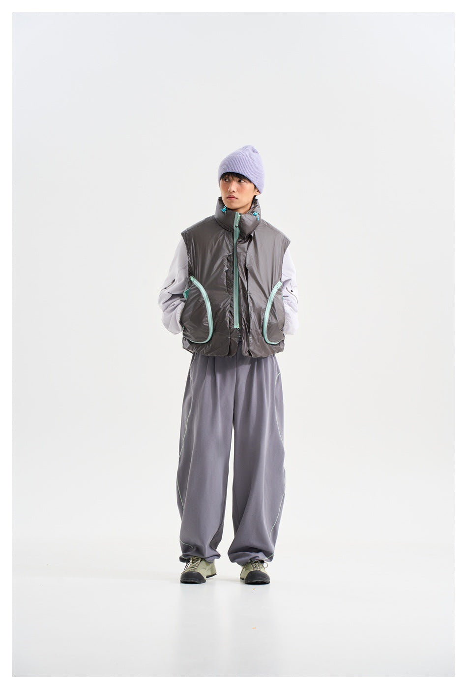 Front view of a model in a charcoal vest with mint-trimmed pockets, white sleeves, gray trousers and lavender beanie.