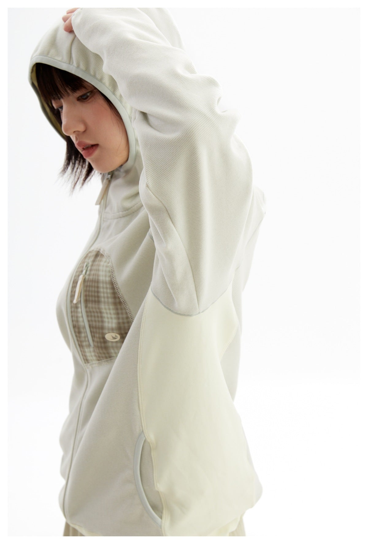 Angled close view of a model wearing an ivory hooded jacket, highlighting its checked zip chest pocket and sleeve.
