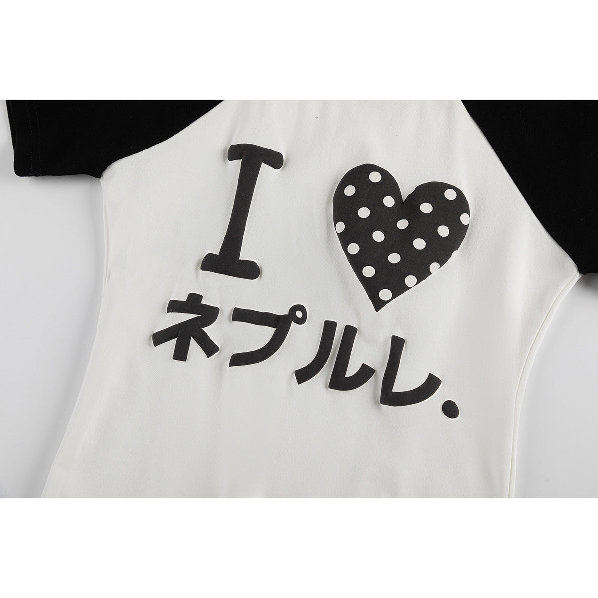 Close-up of a white raglan shirt with black sleeves and a black polka-dot heart graphic with lettering.