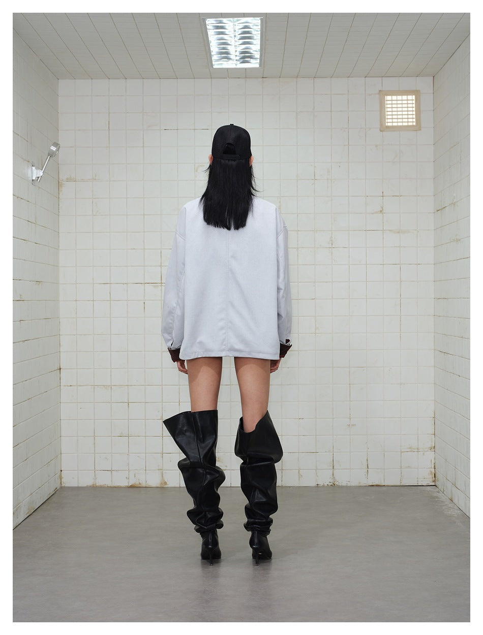 Back view of a model wearing a pale gray jacket with dark cuffs and tall black boots.