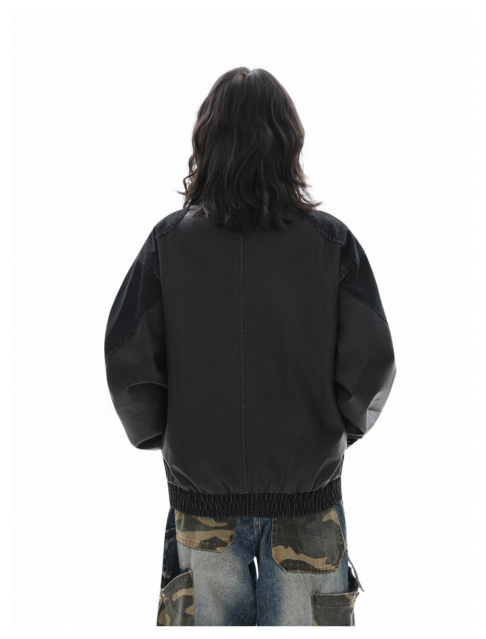 Rear view of a person wearing a black jacket with dark denim shoulder and sleeve panels and a ribbed hem.