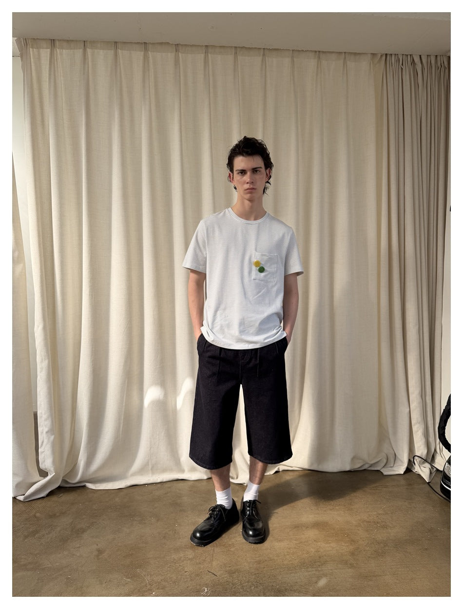 Model facing forward in a white fine-striped T-shirt with yellow and green pocket accents, black shorts and white socks.