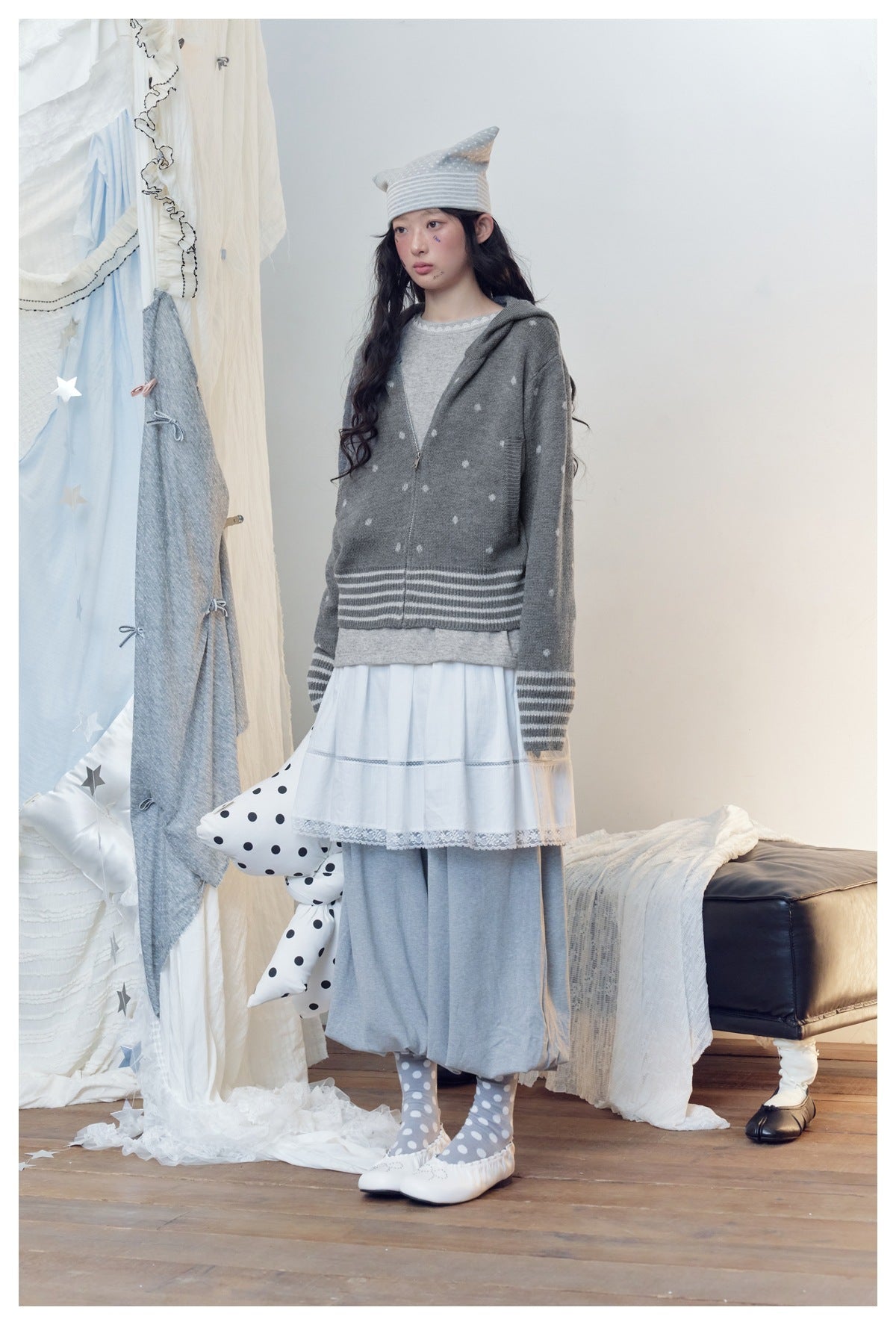 Model in gray polka-dot zip hooded knit jacket with striped cuffs, styled with white skirt and gray pants, three-quarter view