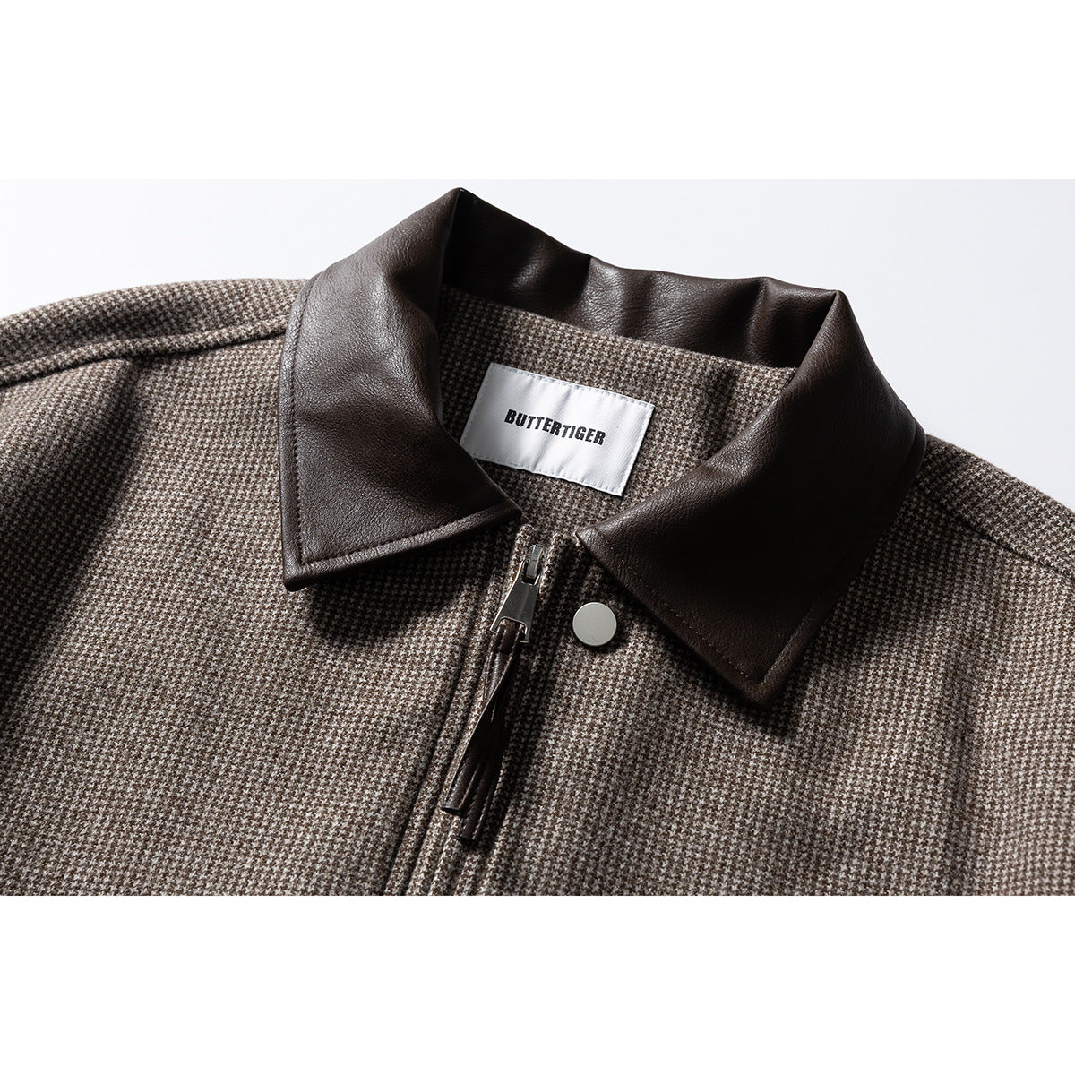 Close-up of a brown-and-cream houndstooth jacket with a dark brown collar, front zipper, snap, and neck label.