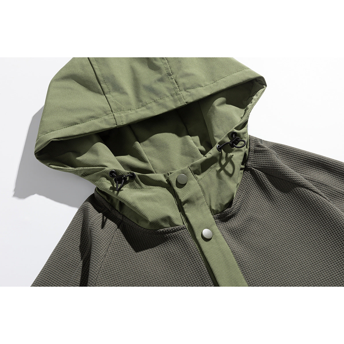 Close-up of an olive hood with black drawcord toggles and snap placket on a dark gray textured pullover.