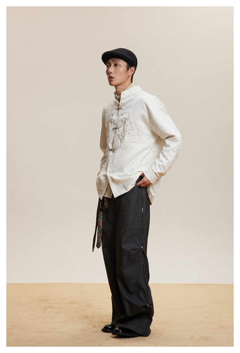 Model in the off-white embroidered shirt with metal frog closures, side view with hands in pockets, dark wide trousers