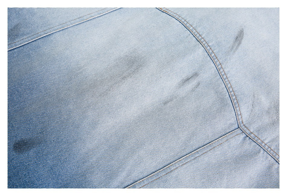 Close-up of light-wash denim fabric with curved double-stitched seams and subtle faded marks.