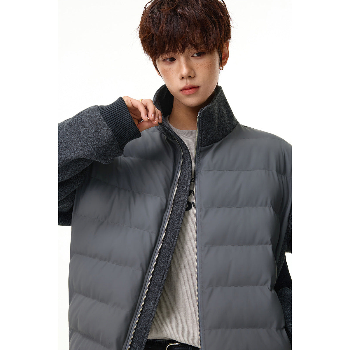 Close view of a model wearing a charcoal-gray quilted zip jacket with textured sleeves and a raised collar.