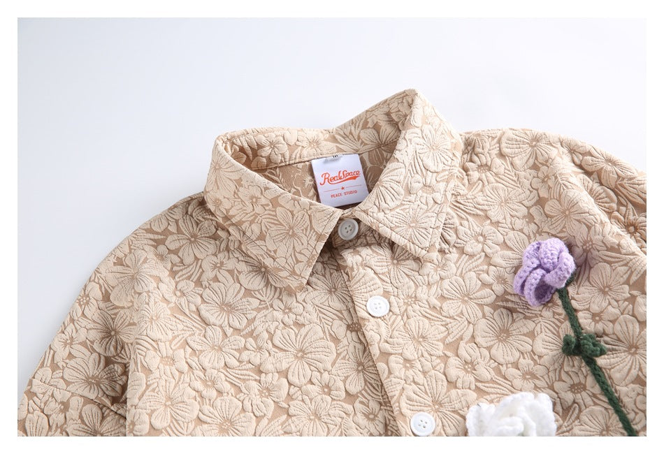 Close-up of a beige floral jacket's collar, buttons, raised texture and purple flower appliqué.