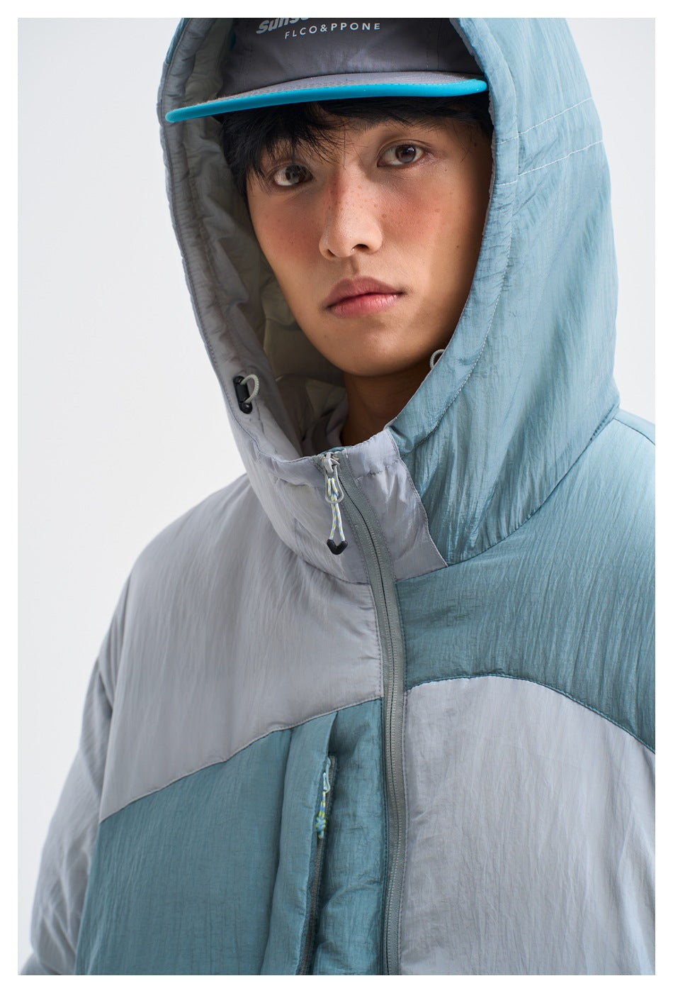 Close-up of the blue-gray jacket's hood, high zip collar, drawcords, and color-blocked front.