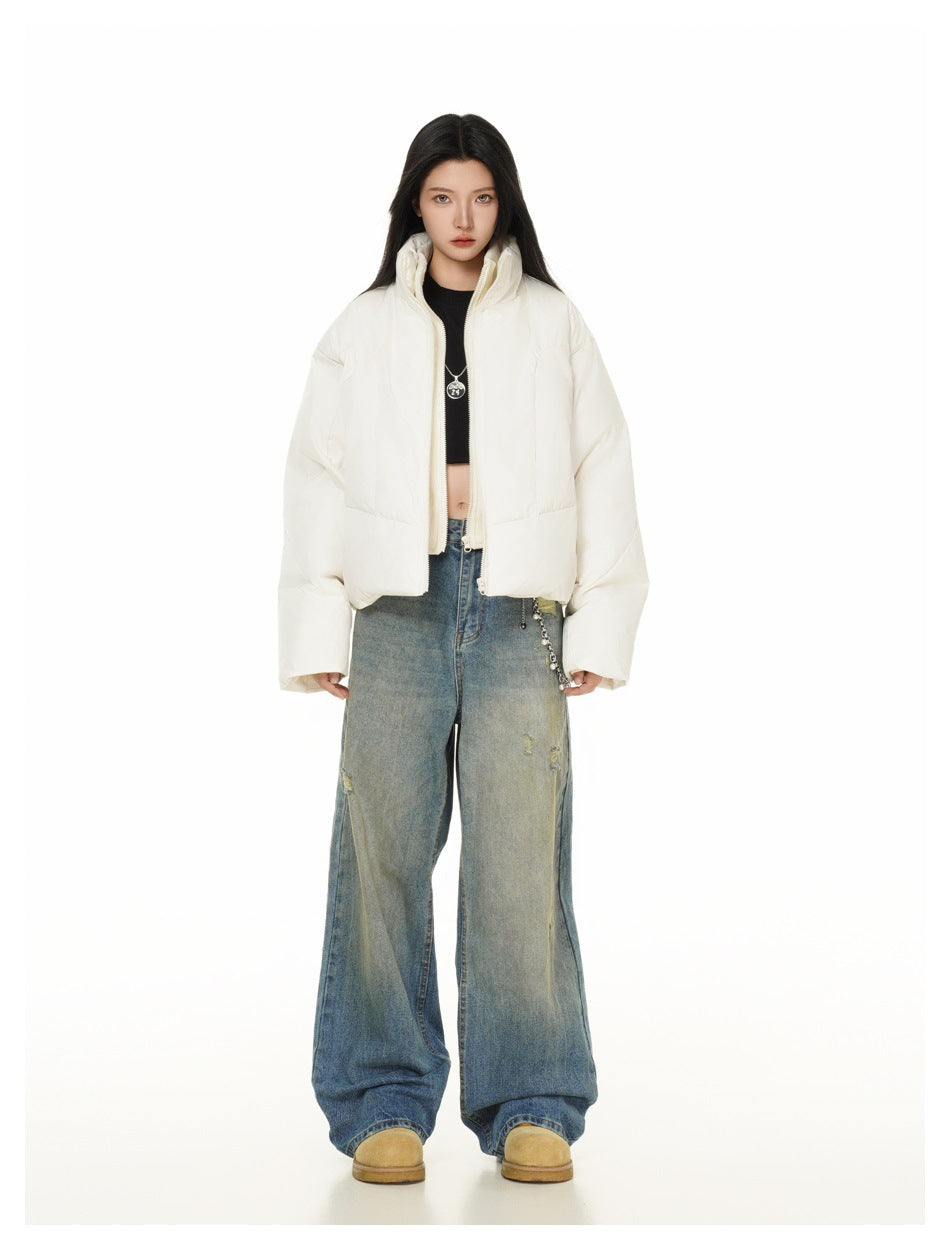 Full-length model wearing an open ivory cropped puffer jacket, wide-leg blue jeans, and tan shoes.