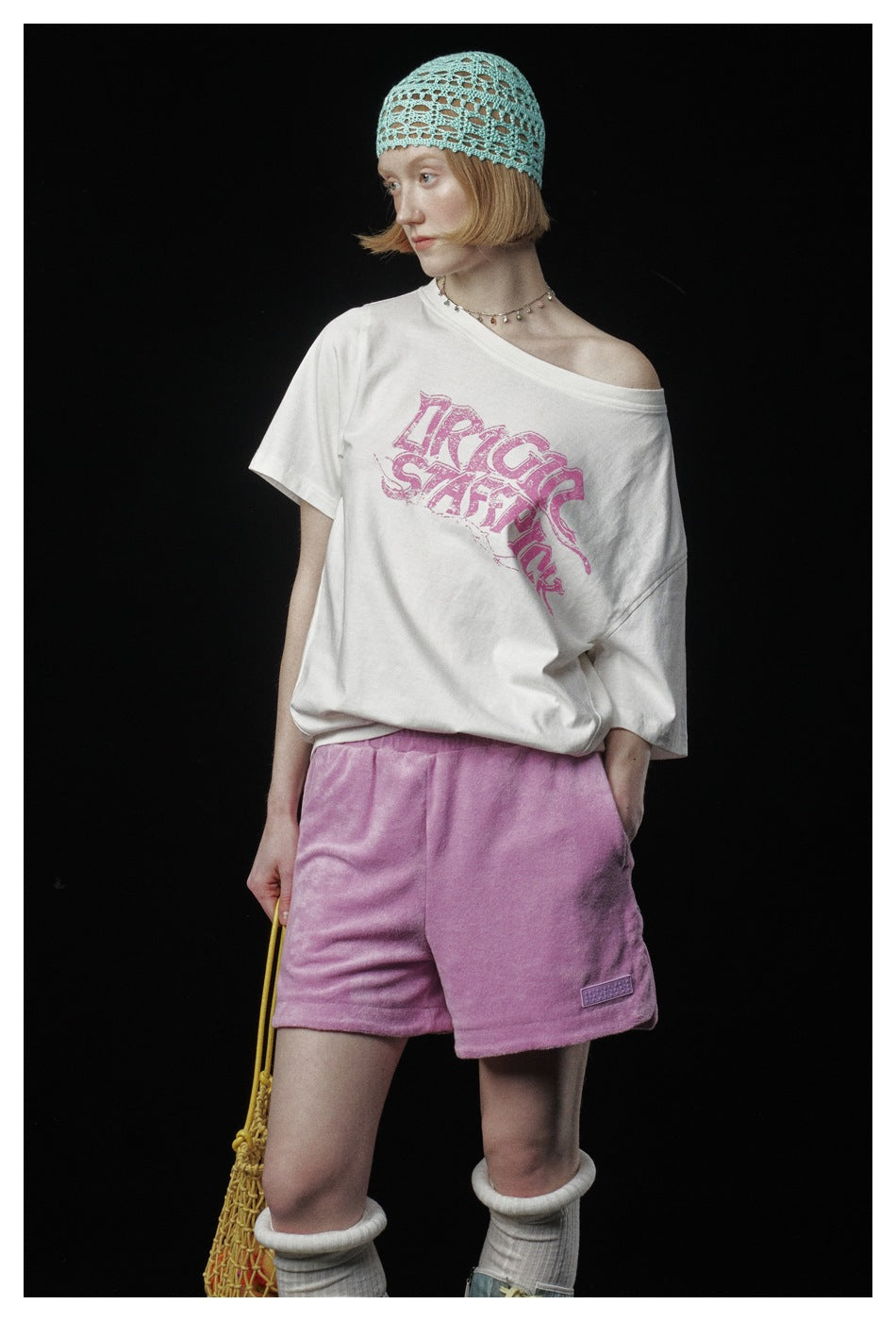 Model wearing an off-white T-shirt with a large pink graphic and pink shorts, shown from the front.