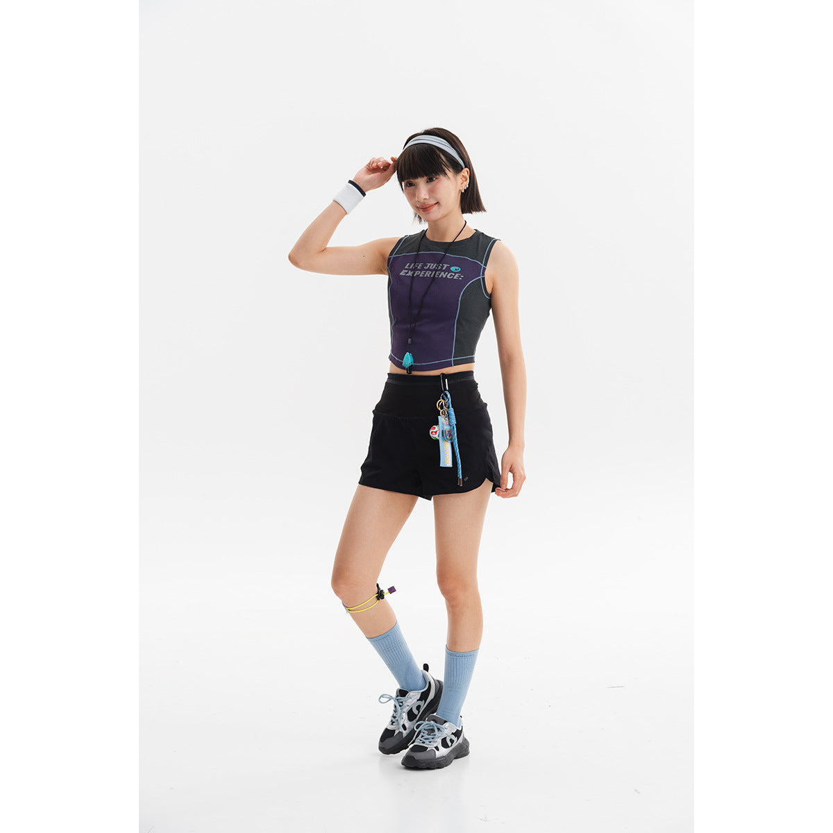 Model wearing a dark cropped athletic tank with blue piping and black running shorts, shown from the front.