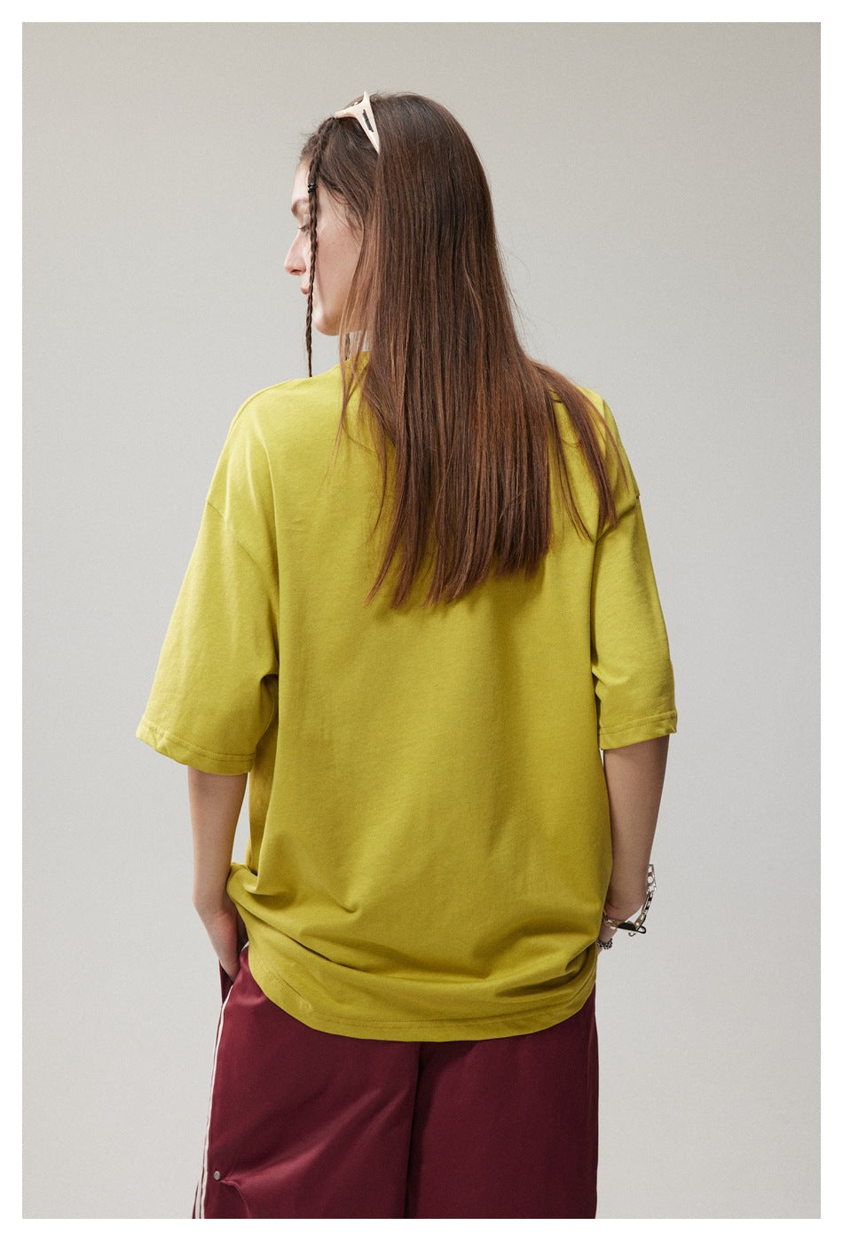 Rear view of a model wearing a plain yellow oversized T-shirt and burgundy pants.