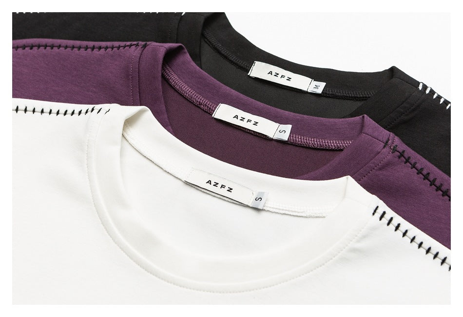 Close-up of white, plum, and black crew-neck shirts with visible neck labels and contrast stitching.