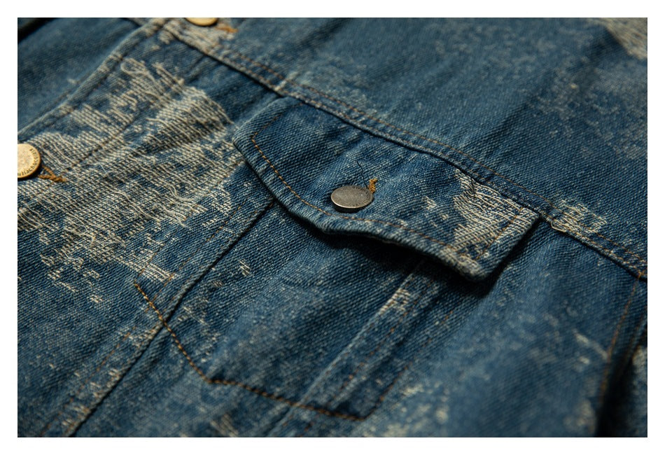 Close-up of a blue denim jacket with a distressed light pattern, flap pocket, and metal button.