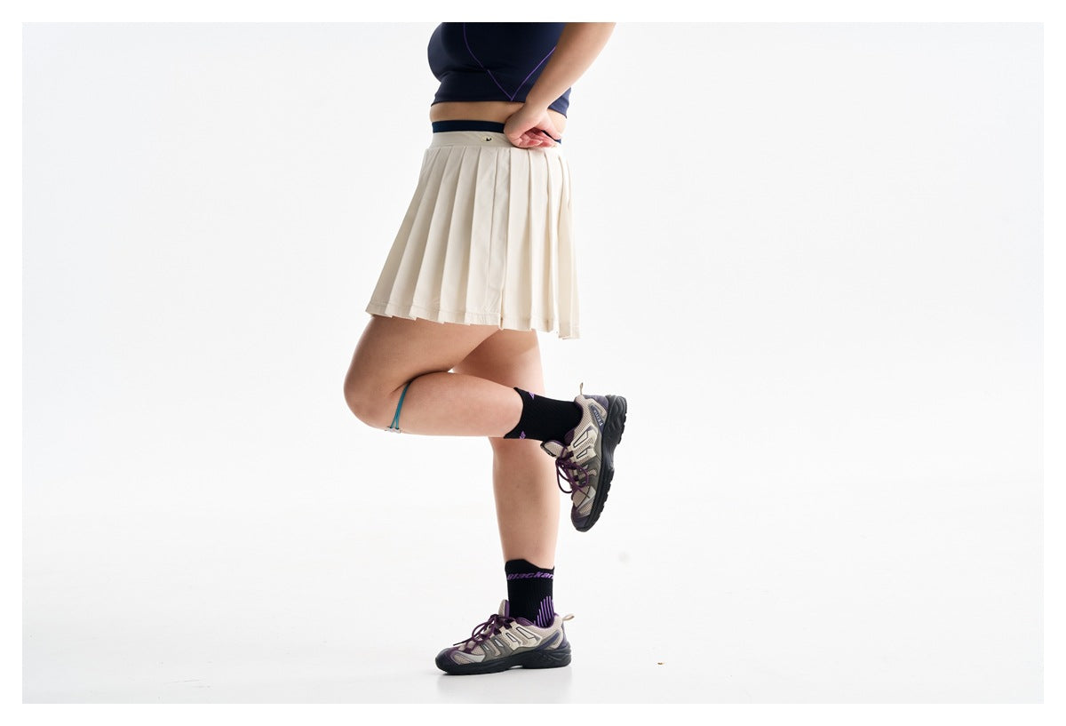 Side view of a model wearing a cream pleated athletic skirt and navy crop top.