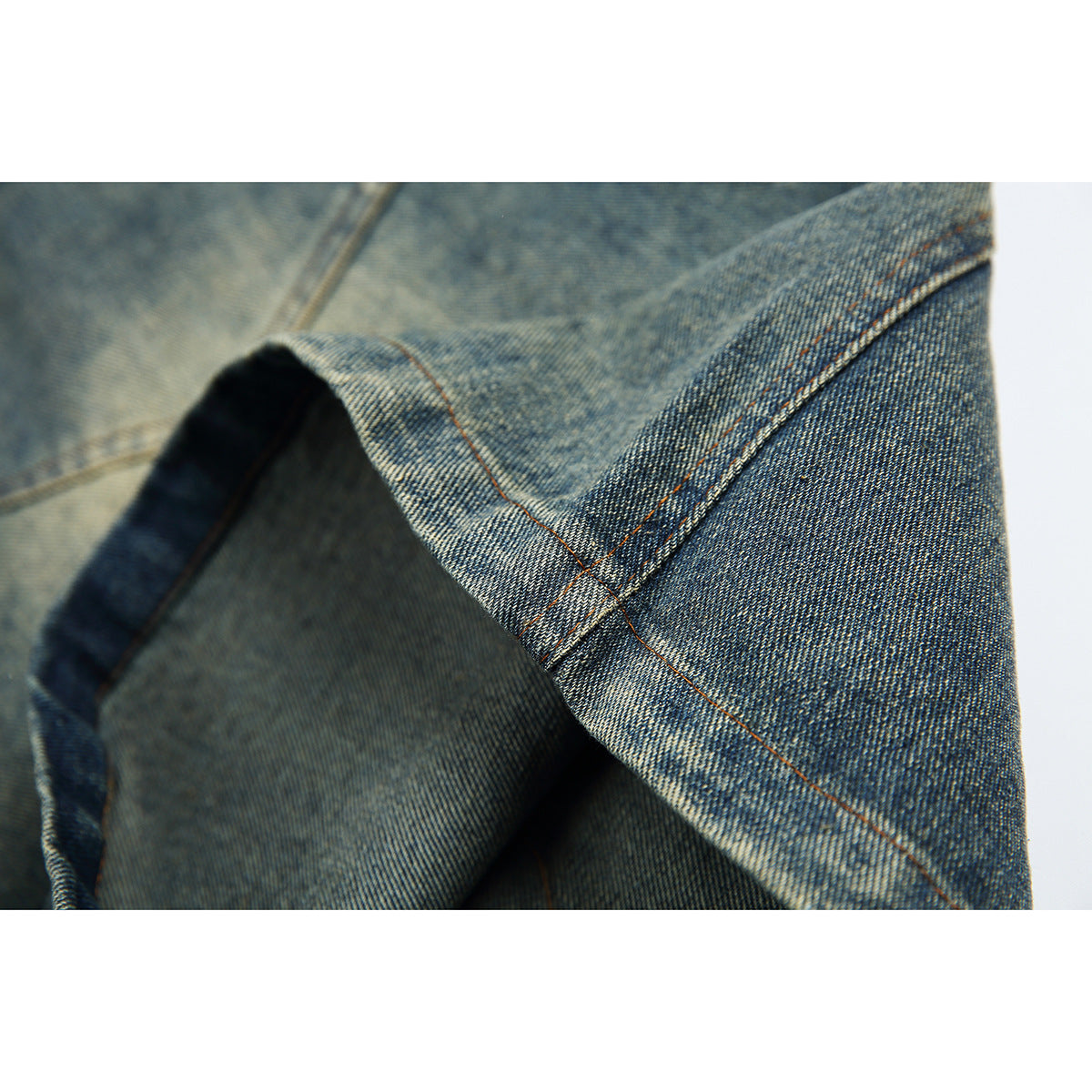 Close-up of a denim shorts hem with visible fabric texture and orange-brown stitching.