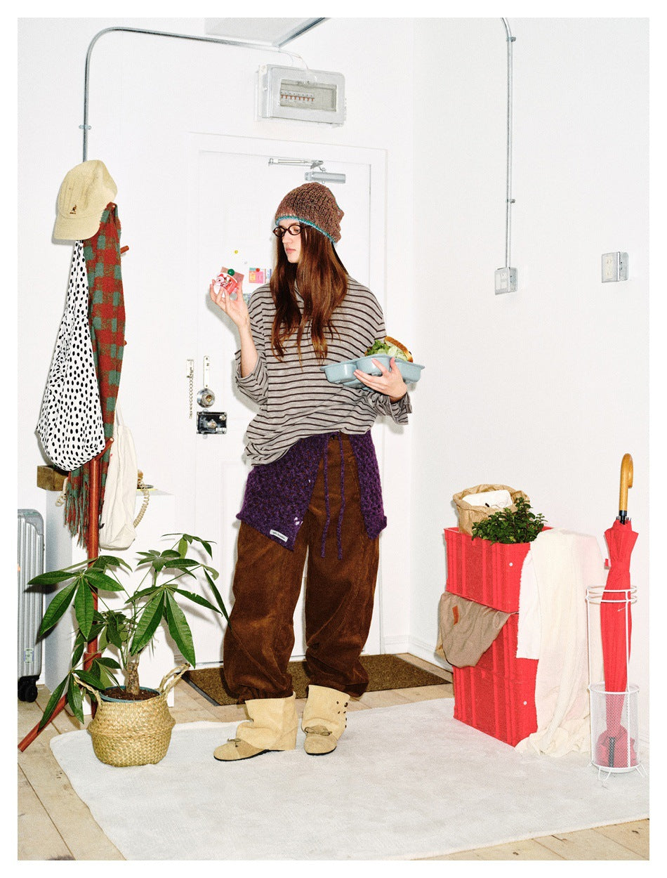 Full-length model wearing an oversized gray-and-black striped henley, brown trousers, and a purple knit wrap.