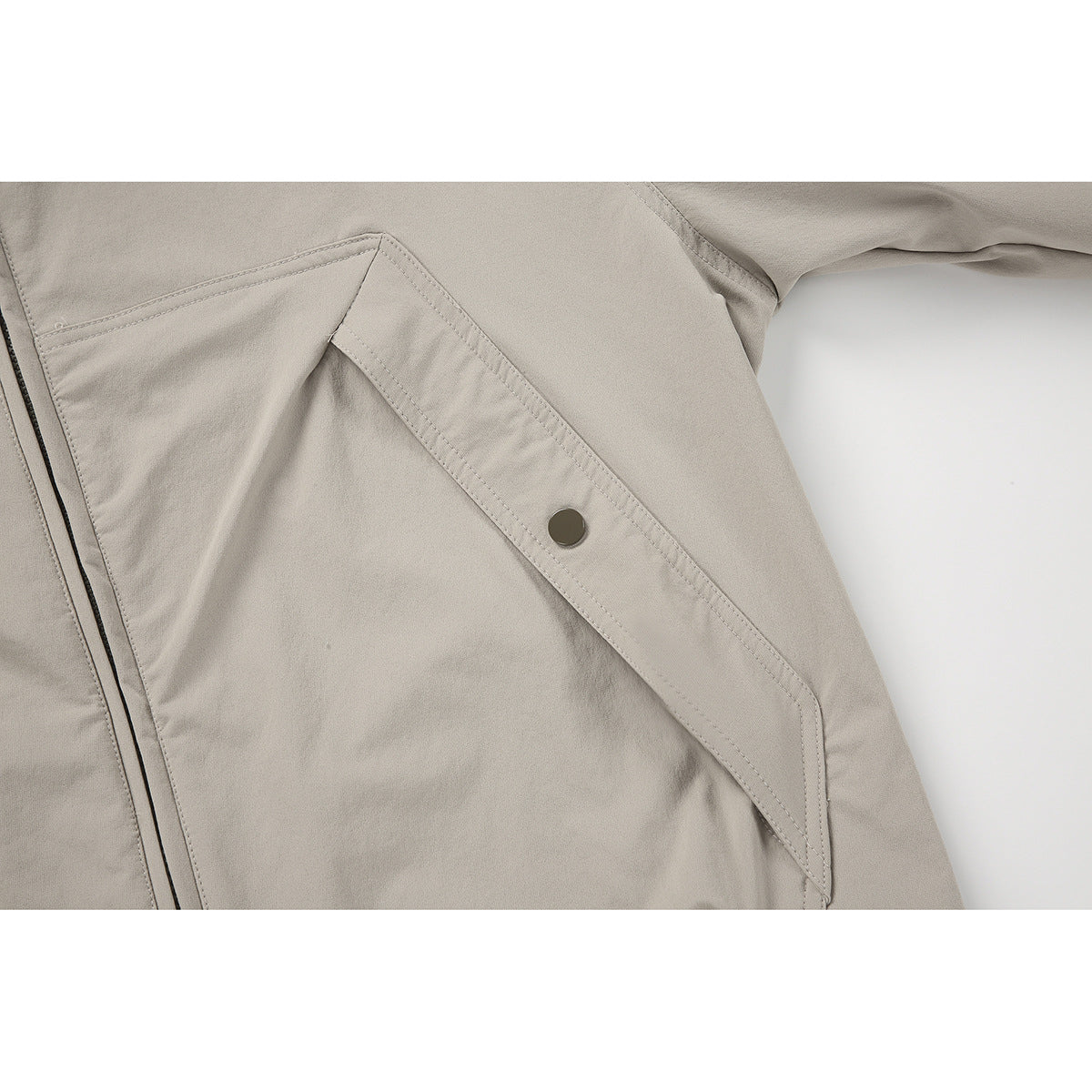 Close-up of a light taupe jacket's angled pocket flap with a dark snap and visible stitching.