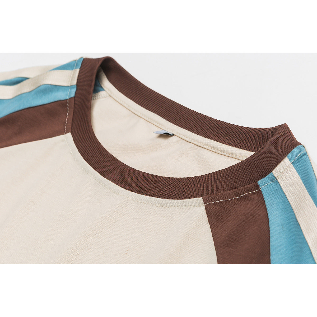 Close-up of a cream raglan T-shirt with a dark brown ribbed crew neck and blue and brown shoulder panels.