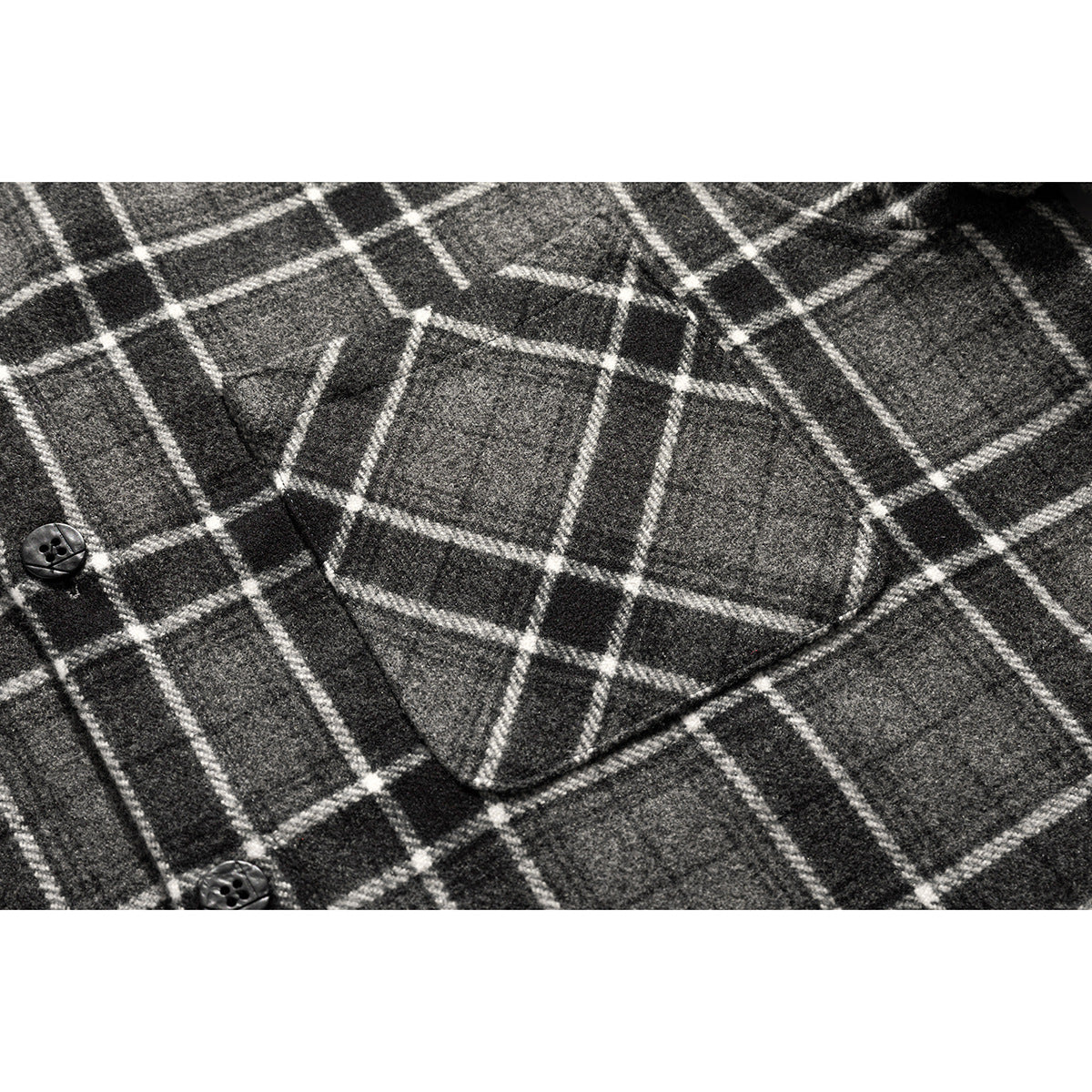 Close-up of a buttoned chest pocket on a charcoal gray shirt with a white plaid pattern.
