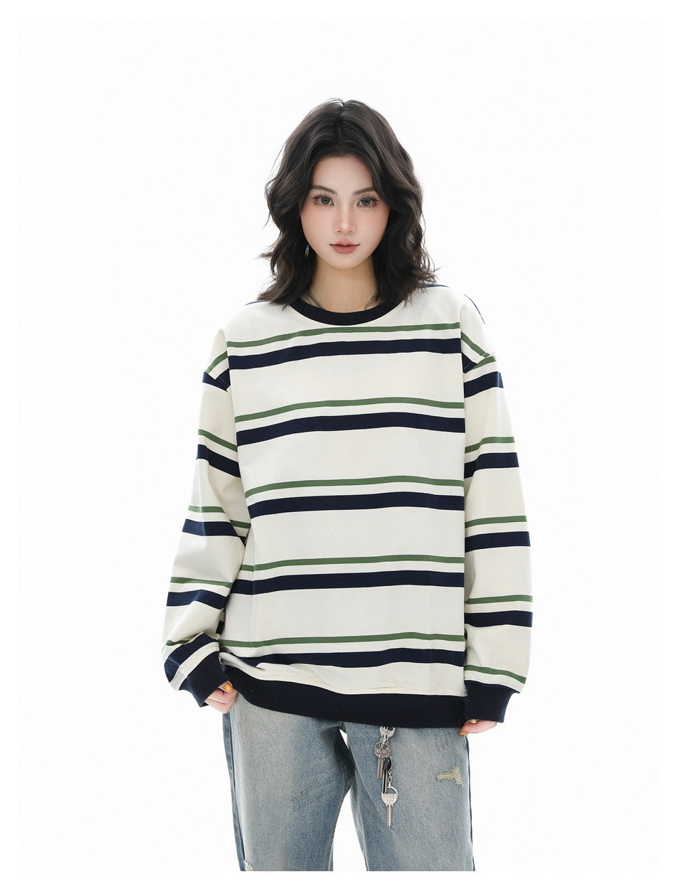 Model wearing an oversized cream sweatshirt with navy and green stripes, navy ribbed cuffs and hem, and light jeans