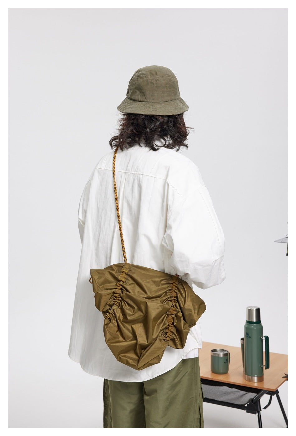 Rear view of a model in a white overshirt carrying a gathered olive-brown shoulder bag.