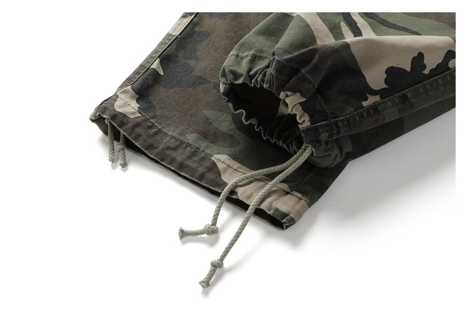 Close-up of olive, black, and tan camouflage pants hem with gathered elastic and dangling drawcords.