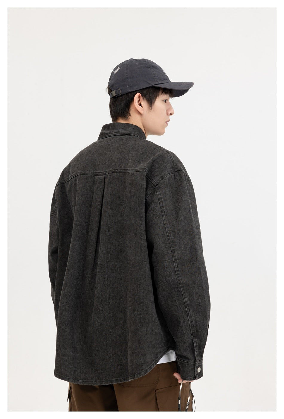 Model viewed from behind wearing a charcoal overshirt with a center-back pleat and curved hem.