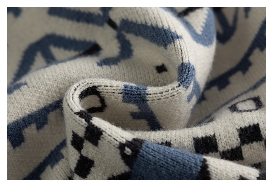 Close-up of folded ivory sweater knit showing a stitched edge and black and dusty blue geometric motifs.