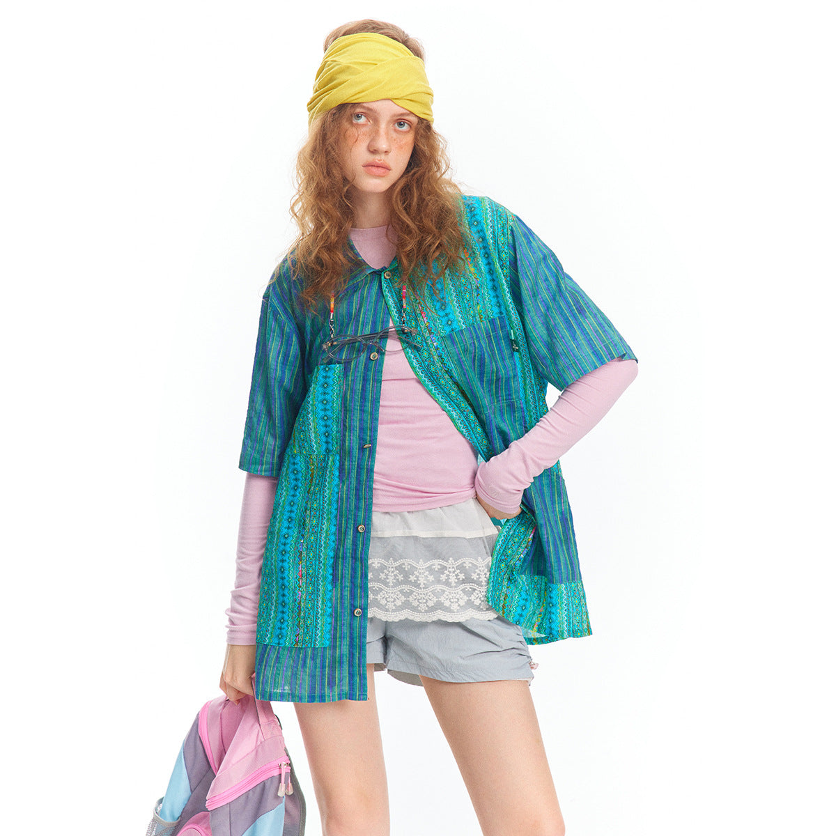 Model wearing a blue and turquoise patterned short-sleeve button-front tunic over pink layers and gray shorts.