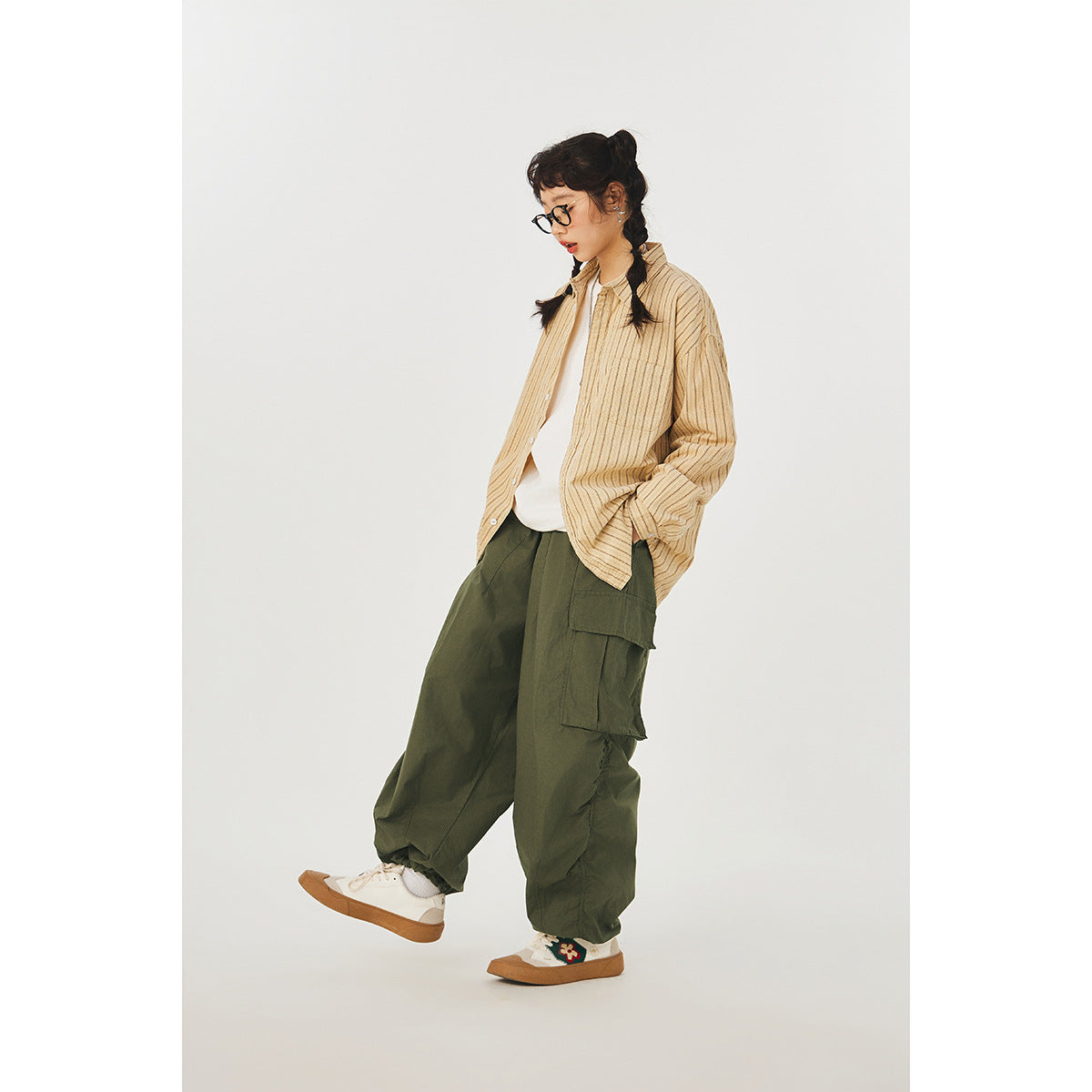 Model wearing loose olive cargo pants with a beige striped overshirt and white sneakers.