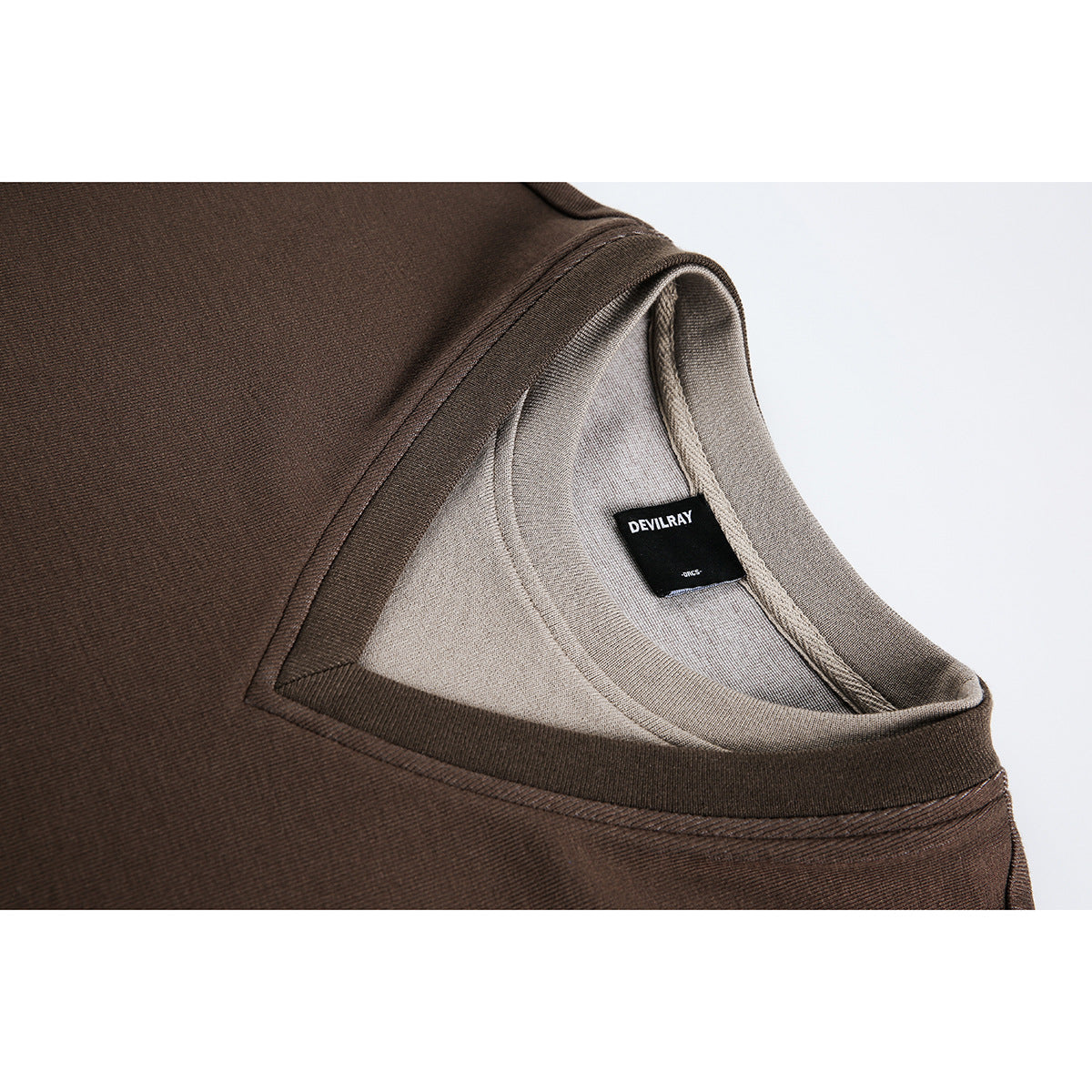 Close-up of a brown top's layered neckline and interior, showing a black DEVILRAY neck label.